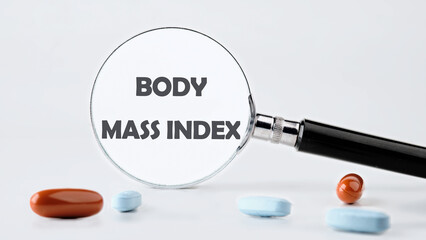 Wall Mural - Business concept acronym. BMI. Body Mass Index through a magnifying glass on a gray background in a composition with tablets and vitamins. Concept photo