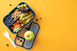 © ActionGP - Healthy school snack in lunchbox with fresh fruits, vegetables, nuts, and sandwich arranged on yellow background