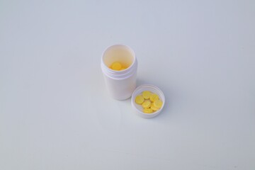 Yellow colored medicine tablets or vitamin C medication spilling from the bottle in close up view on white background.