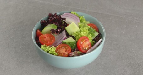 Wall Mural - Healthy salad of fresh vegetables in a plate on a gray background. Close-up footage on the rotating table.