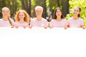 Wall Mural - Diverse Ladies Breast Cancer Volunteers In Pink T-Shirts Holding Empty White Board For Text Standing Outdoor. Mockup