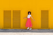 © VISTA by Westend61 - Woman with curly hair walking across yellow wall