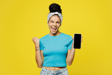 Wall Mural - Young winner Latin woman she wears blue top t-shirt headband casual clothes hold in hand use mobile cell phone with blank screen workspace area isolated on plain yellow background. Lifestyle concept.