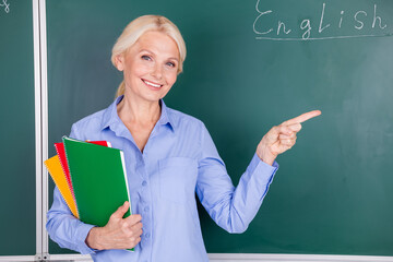 Wall Mural - Photo of charming happy lady senior woman hand hold scientific materials english course isolated on green board background