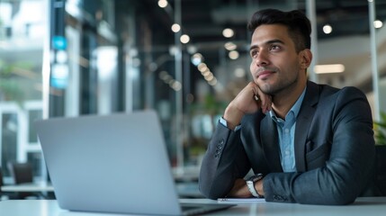 Poster - A man in a suit is sitting at a desk with a laptop open in front of him