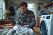 © AISTEL - Young man is putting clothes in the washing machine, doing laundry at home in modern laundry room .