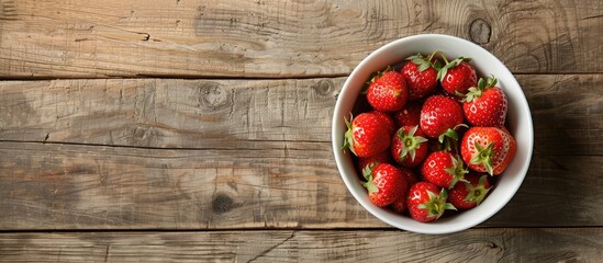 Poster - A top view copy space image features fresh strawberries in a white bowl on a rustic wooden table