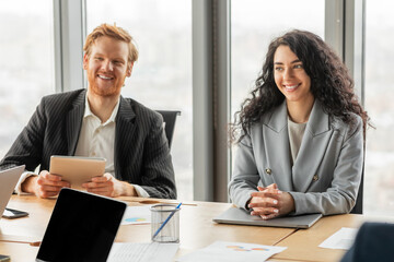 Aufkleber - Two businesspeople, a man and a woman, are seated at a table in a modern office setting. They are both smiling and appear to be engaged in a conversation