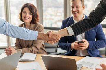 Aufkleber - Two people are sitting at a table in a modern office. One person, a man in a blue shirt, is shaking the hand of another person, a man in a suit.