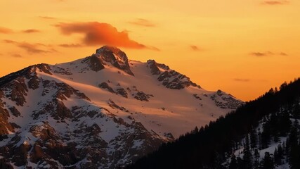 Poster - As the sky turns a deep shade of orange the snowcovered peaks bask in its warm glow.