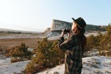 Wall Mural - Woman in plaid shirt and hat capturing majestic mountain view with camera on bright sunny day