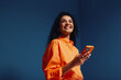 © Jacob Lund - Happy gen z woman using phone in vibrant orange monochromatic setting against blue background
