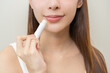 © KMPZZZ - Lip care protection concept, pretty asian young woman, girl hand applying lipstick balm with moisturising on dry mouth from natural beauty product, skincare routine, makeup and cosmetics on background