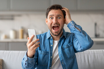 Poster - A man in a blue button-down shirt sits on a couch, looking shocked while holding a smartphone in his left hand and holding his right hand to his head. His mouth is open in surprise.