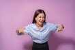 © amnaj - Asian businesswoman with a wide smile pointing down with both index fingers against a vibrant purple background