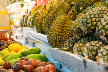 Variety of fresh tropical fruits displayed at a market stall. Colorful display of fresh durians, pineapples, , mango and passion fruits at Phuket market, Thailand