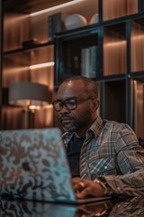 Poster - A man wearing glasses is sitting at a desk and using a laptop. Concept of focus and concentration as the man works on his computer. The man's attire, including the plaid shirt and glasses