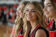 © naravadee - Four smiling cheerleaders in red and black uniforms sit on the sidelines of a basketball game.