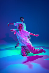 Canvas Print - Talented young man and woman in casual sports clothes dancing hip-hop against purple studio background in neon light. Dance show. Concept of contemporary dance, hobby, youth