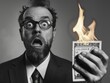 © MK - A person holds a burning dollar bill, conveying frustration or anger