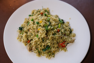 Green curry fried rice with long beans, basil leaves, corn, and meat served in a white plate.