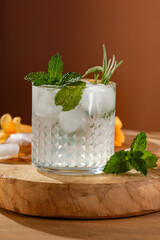 Wall Mural - Cold brew water drink with ice cubes and fresh rosemary and mint leaves. Yellow lemons and copy space on wooden table. 