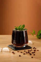 Wall Mural - Cold brew coffee water drink with ice cubes and  fresh mint leaves on wooden table and brown background.  