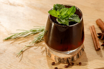 Wall Mural - Cold brew coffee water drink with ice cubes and  fresh mint leaves on wooden table and brown background.  