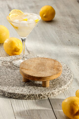 Wall Mural - Water with lemon and ice cubes in cocktail glass, mocktail and lemons scattered on wooden table. Copy space for products.