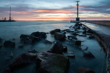 Wall Mural - a small marina on a lake. Breakwater and pillar with golden figure in the dreamy sunset. Landscape shot in Siófok, Balaton, Hungary