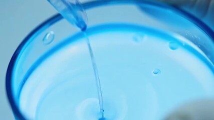 Poster - A close-up view of a glass dropper releasing blue liquid into a clear container.