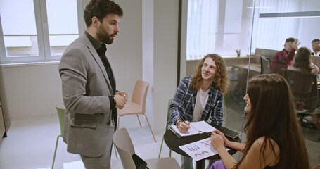 Wall Mural - Young employees working together on a project in a start-up office, discussing marketing growth, profitability, and market analysis.