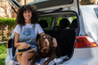 © zinkevych - Cute curly-haired young woman sitting in the car with the dog ands looking happy