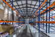 © alhim - Organized Warehouse Interior Featuring High Racks and Labeled Boxes. The spacious warehouse is filled with tall shelving units, stacked with neatly labeled boxes. Bright overhead lights illuminate
