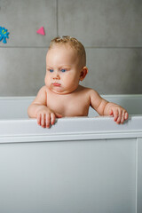 Wall Mural - A blue-eyed baby with a bare torso is standing in the bathroom and smiling. Emotions of joy in a baby. Baby's personal hygiene.