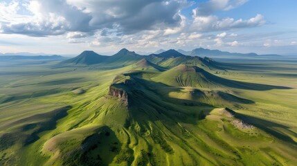 Aufkleber - A vast, green field with a mountain range in the background. The mountains are covered in grass, giving the scene a peaceful and serene atmosphere. The combination of the open field