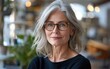 © imagineRbc - A mature woman with grey hair and glasses smiles warmly while seated in a bright, inviting co-working space filled with natural light