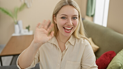 Sticker - A cheerful young caucasian woman is waving hello in a bright cozy indoor home setting.