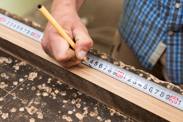 The carpenter measures the distance with a pencil using a tape measure