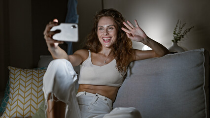 Wall Mural - A joyful caucasian woman takes a selfie on a smartphone in a cozy living room.