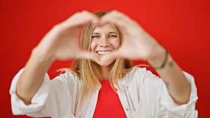 Poster - Smiling young blonde woman making a heart shape with her hands against a red background