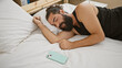 © Krakenimages.com - A bearded young hispanic man sleeps peacefully in a bedroom, his smartphone resting beside him on the white sheets.