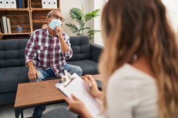 Sticker - Pensive, mature man with grey hair mired in thought, masked and seated at a psychology clinic, hand on chin, mulling serious queries and ideas