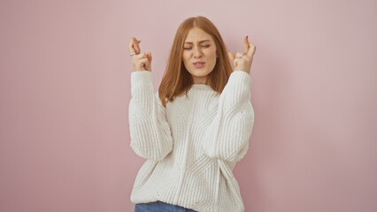 Canvas Print - Hopeful young woman in sweater crossing fingers for luck against a pink background