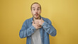© Krakenimages.com - Bald hispanic man with beard in denim shirt over yellow background making surprised expression.