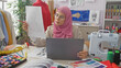 © Krakenimages.com - A focused woman reviews a dress design in a colorful tailoring studio, surrounded by fabric, a sewing machine, and pattern samples.