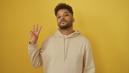 A confident adult black man makes the number three gesture against an isolated yellow background.