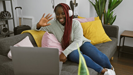 Canvas Print - A cheerful black woman with braids making a video call from her cozy, plant-decorated living room at home.