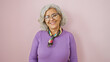 © Krakenimages.com - A cheerful middle-aged woman with glasses and grey hair, dressed in purple, stands before a pink background.