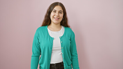 Portrait of a smiling young hispanic woman wearing a turquoise sweater isolated against a pink wall.